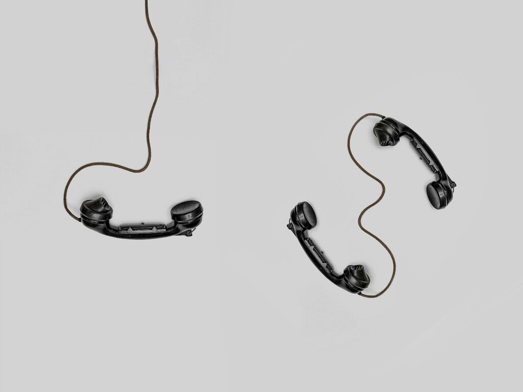 An image with 3 hand help black phones with cords spread across the floor.