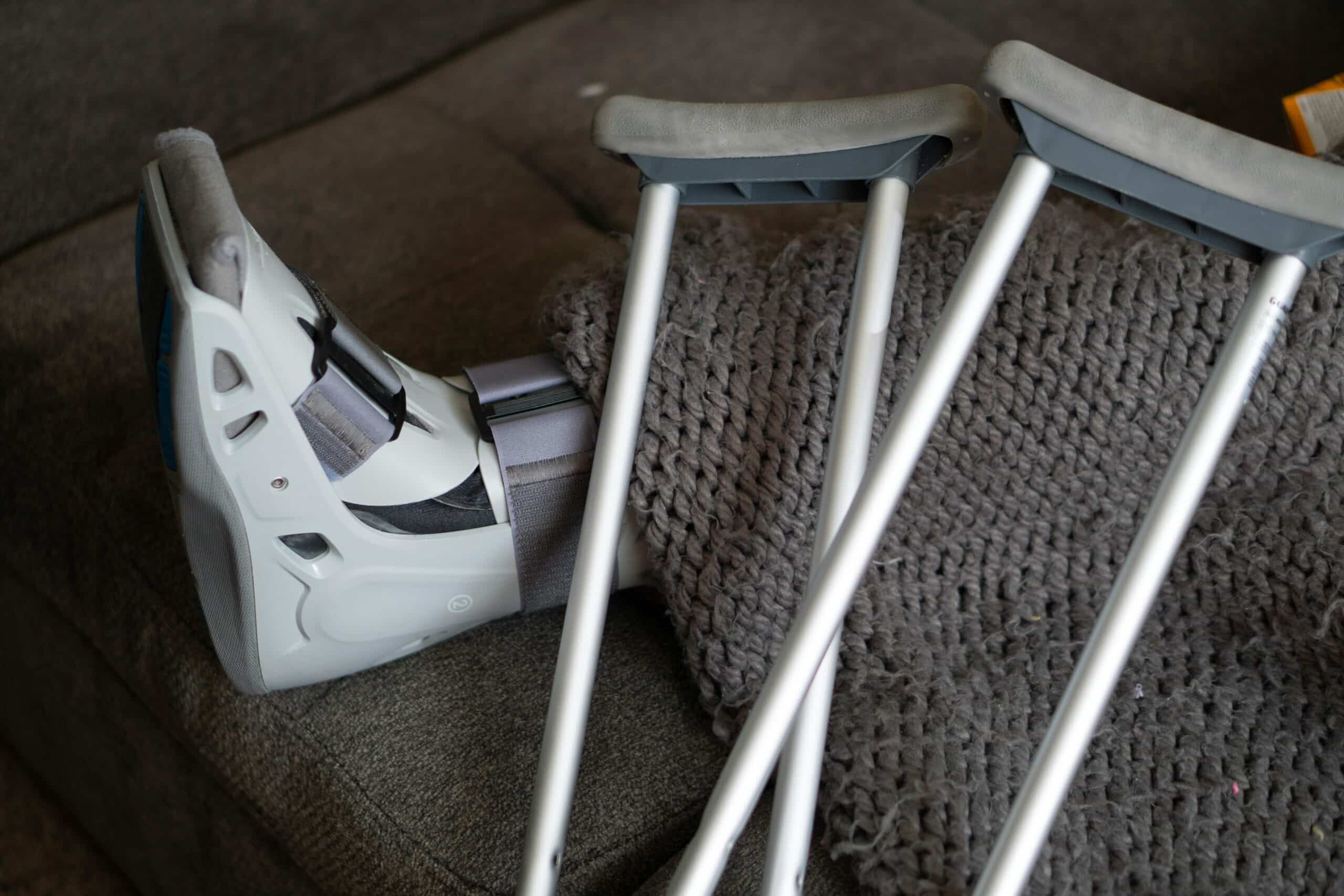 A foot resting in a moon boot on a couch which crutches next to foot indicating an injury or break to foot.